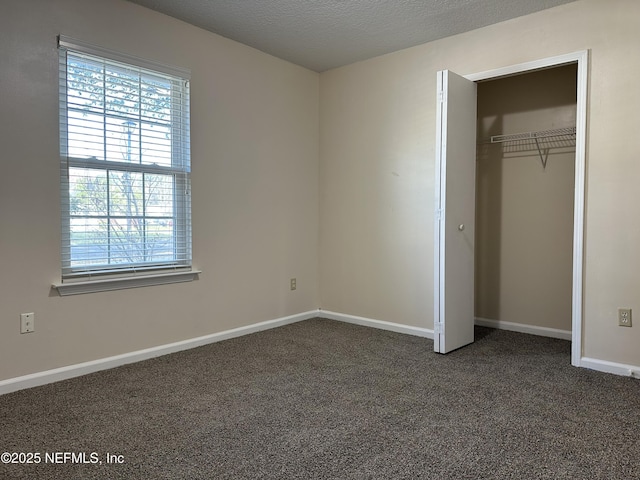 unfurnished bedroom with a textured ceiling, dark carpet, and a closet