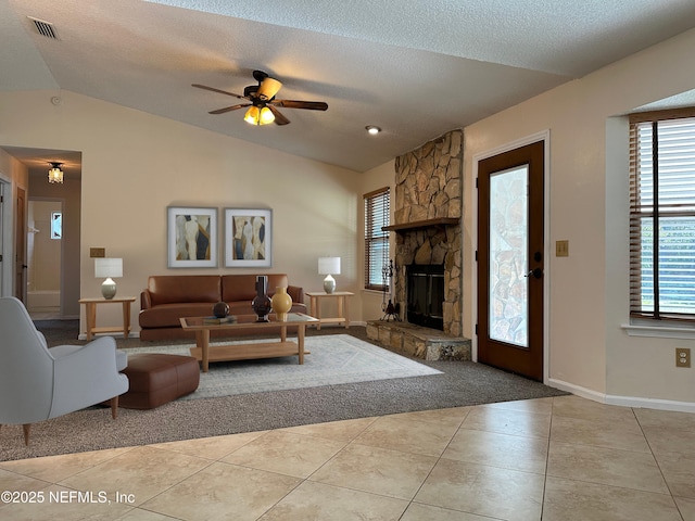 tiled living room with ceiling fan, a stone fireplace, vaulted ceiling, and a textured ceiling