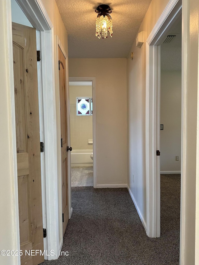 hallway featuring a textured ceiling and dark carpet