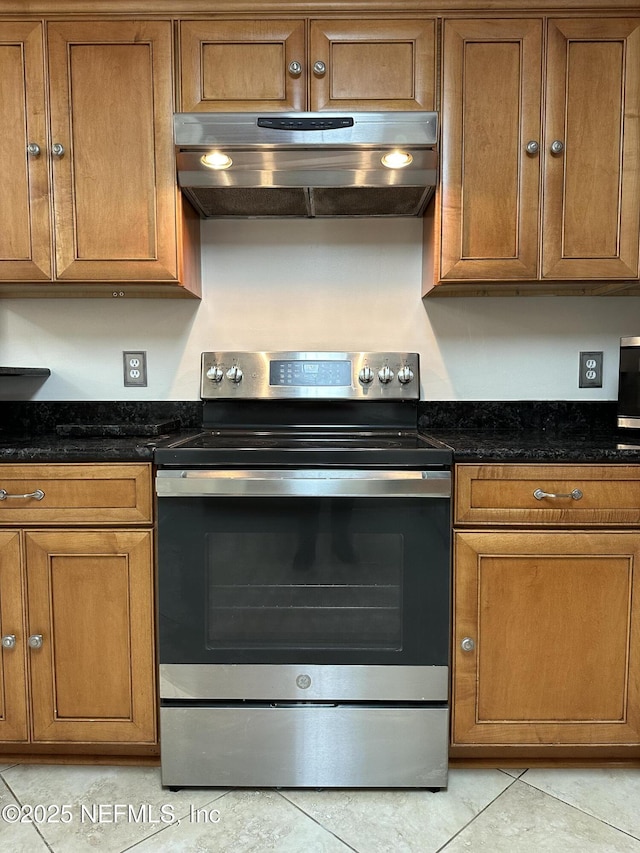 kitchen with dark stone countertops, light tile patterned floors, and electric range