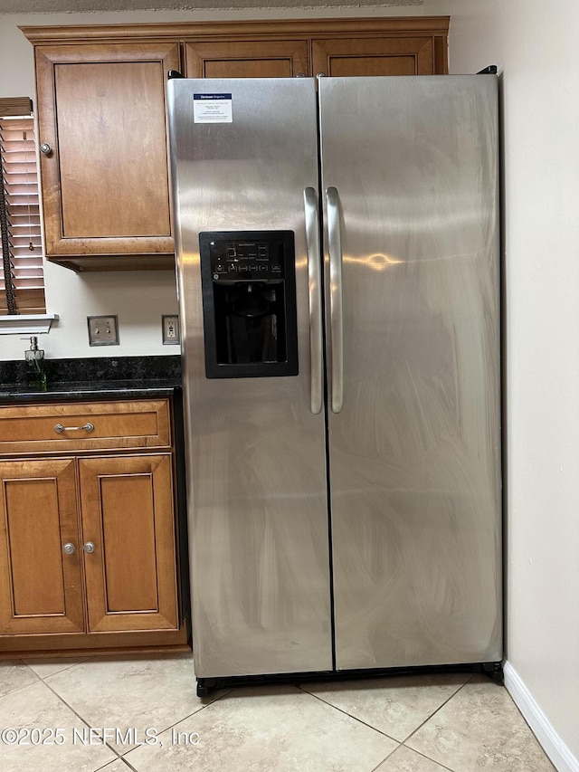 kitchen with light tile patterned floors, dark stone counters, and stainless steel refrigerator with ice dispenser