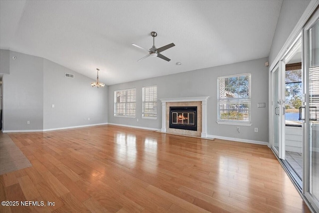 unfurnished living room with ceiling fan with notable chandelier, lofted ceiling, a fireplace, and light hardwood / wood-style floors