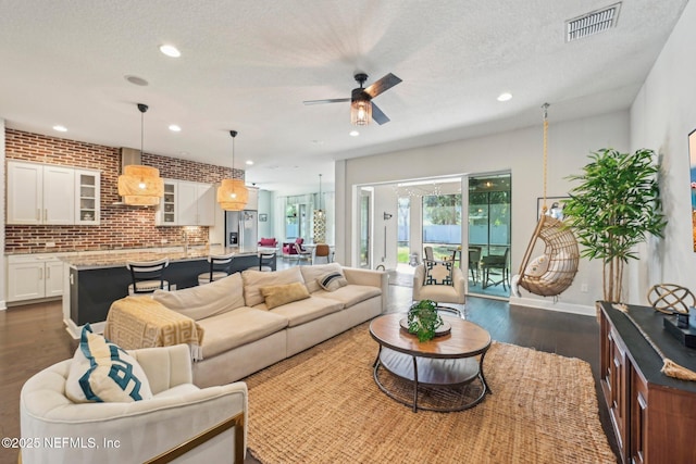 living room featuring ceiling fan, brick wall, dark hardwood / wood-style floors, and a textured ceiling