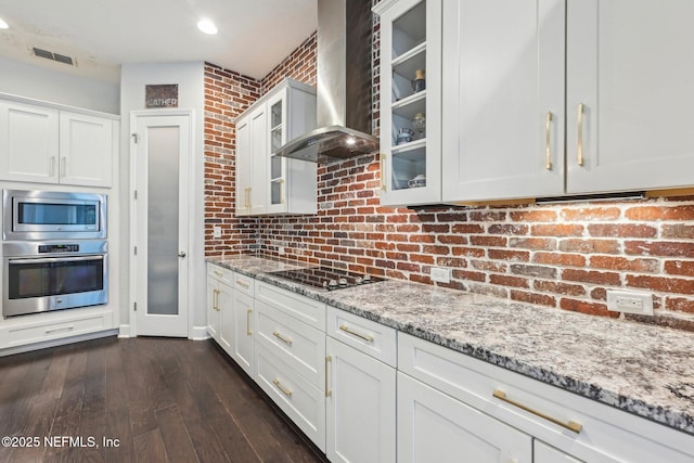 kitchen featuring stainless steel appliances, light stone countertops, wall chimney range hood, and white cabinets