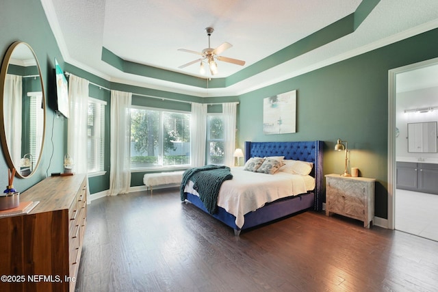 bedroom with dark wood-type flooring, connected bathroom, ornamental molding, a raised ceiling, and ceiling fan