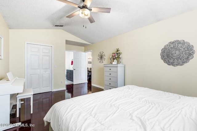 bedroom with dark wood-type flooring, lofted ceiling, a textured ceiling, a closet, and ceiling fan