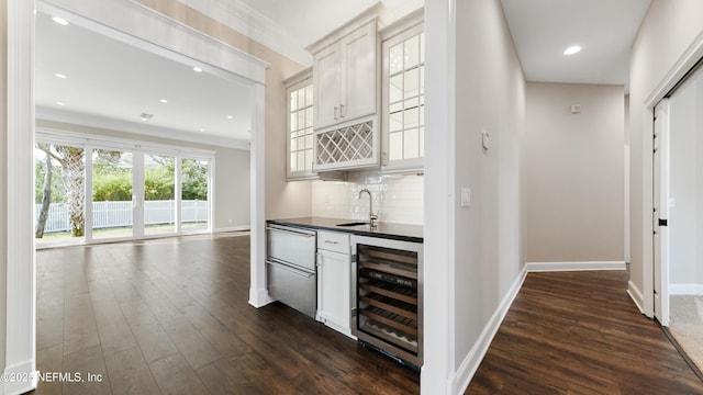 bar with dark wood-type flooring, sink, white cabinetry, beverage cooler, and backsplash