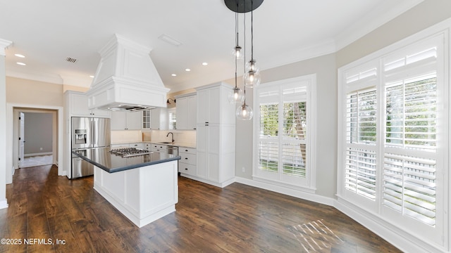 kitchen featuring pendant lighting, premium range hood, white cabinetry, stainless steel appliances, and a center island