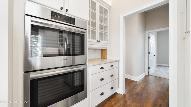 kitchen with dark wood-type flooring, white cabinetry, tasteful backsplash, double oven, and light stone countertops