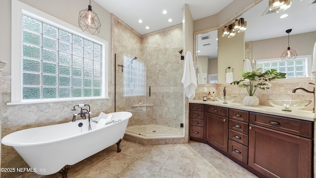 bathroom featuring plus walk in shower, plenty of natural light, tile walls, and vanity