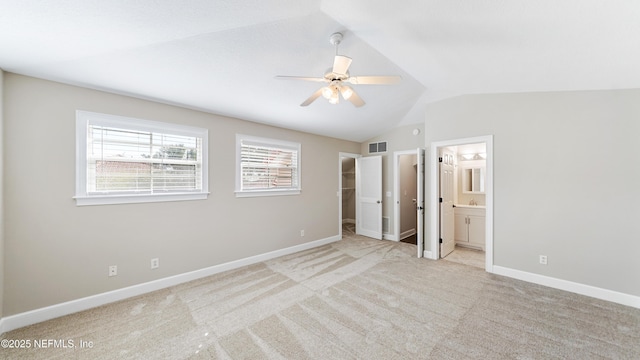 unfurnished bedroom with vaulted ceiling, a spacious closet, ceiling fan, light carpet, and ensuite bath