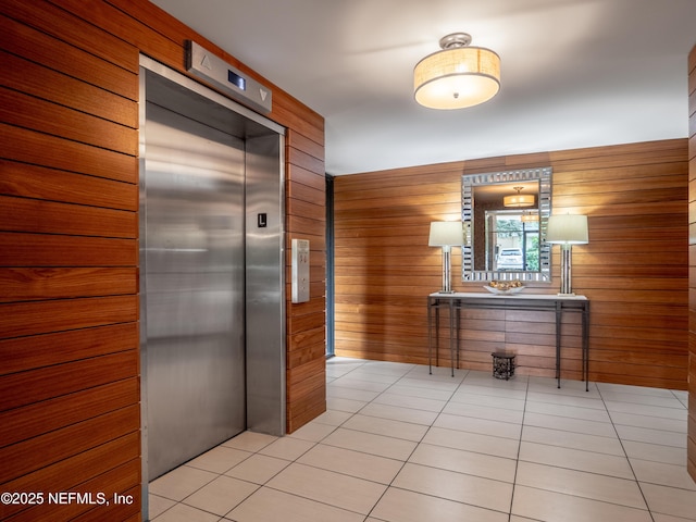 corridor with elevator, light tile patterned floors, and wood walls