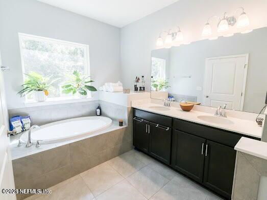 bathroom with tile patterned flooring, tiled tub, and vanity