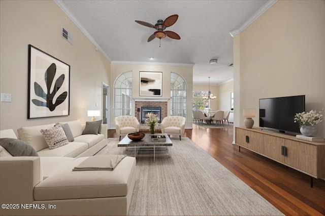 living room with crown molding, dark wood-type flooring, a fireplace, a textured ceiling, and ceiling fan with notable chandelier