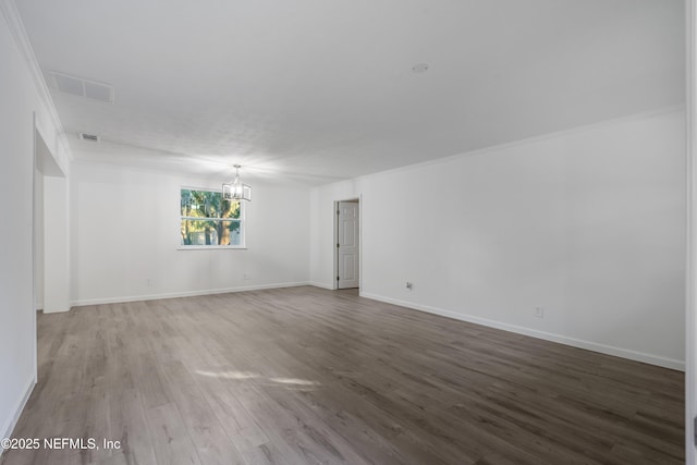 empty room featuring wood-type flooring, ornamental molding, and a chandelier