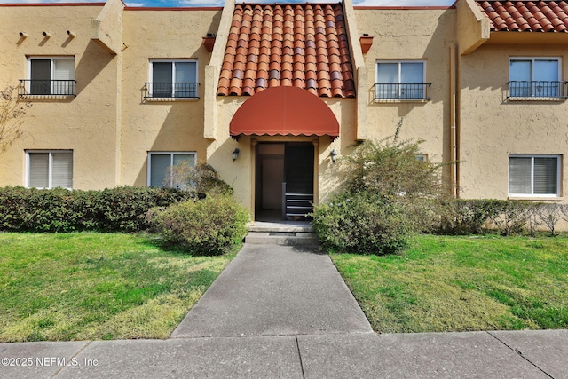 view of front facade with a front yard, a tile roof, and stucco siding