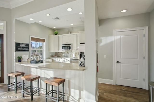 kitchen with appliances with stainless steel finishes, white cabinetry, backsplash, a kitchen breakfast bar, and kitchen peninsula