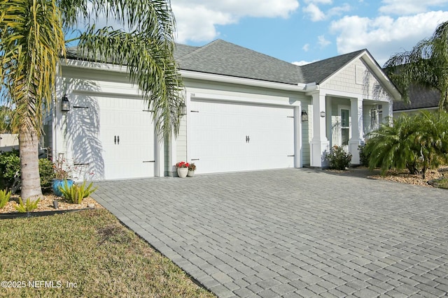 view of front of property with a shingled roof, decorative driveway, and an attached garage