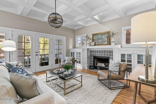 living room with beamed ceiling, a tile fireplace, light hardwood / wood-style flooring, and french doors