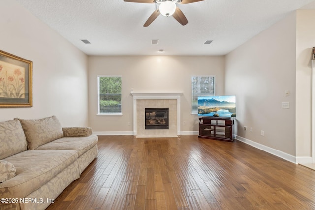 living room featuring ceiling fan, dark hardwood / wood-style floors, a tile fireplace, and a textured ceiling