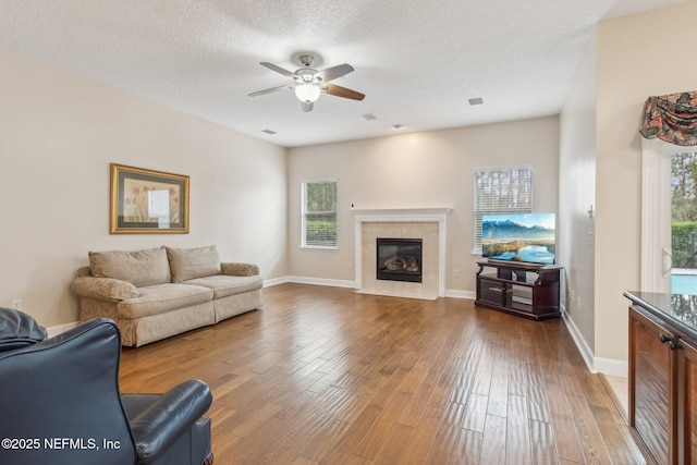 living room featuring wood-type flooring, a tiled fireplace, and a textured ceiling