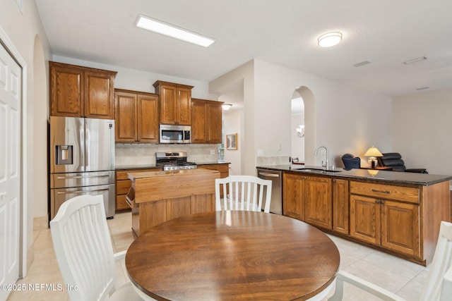 kitchen featuring sink, light tile patterned floors, appliances with stainless steel finishes, decorative backsplash, and kitchen peninsula