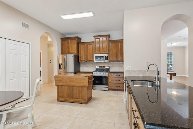 kitchen with sink, a center island, dark stone counters, stainless steel appliances, and decorative backsplash