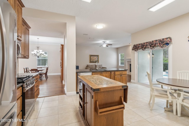 kitchen featuring light tile patterned flooring, a kitchen island, appliances with stainless steel finishes, ceiling fan with notable chandelier, and sink