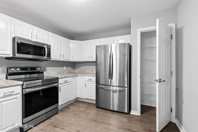 kitchen with hardwood / wood-style floors, a textured ceiling, white cabinets, and appliances with stainless steel finishes