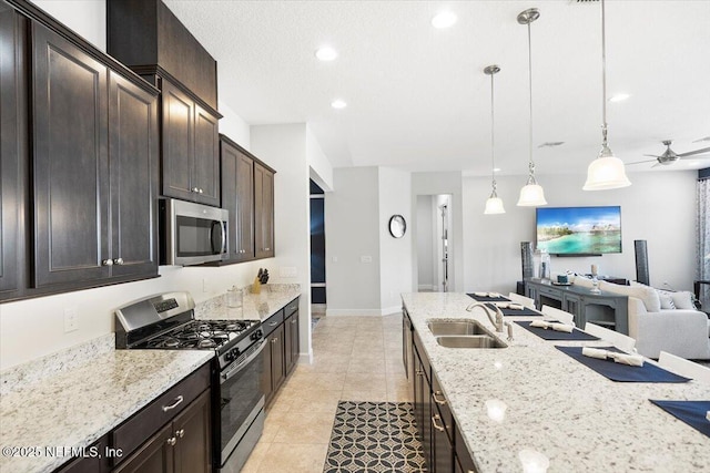 kitchen with sink, dark brown cabinets, pendant lighting, stainless steel appliances, and light stone countertops