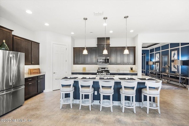 kitchen with a kitchen island with sink, hanging light fixtures, stainless steel appliances, and dark brown cabinetry