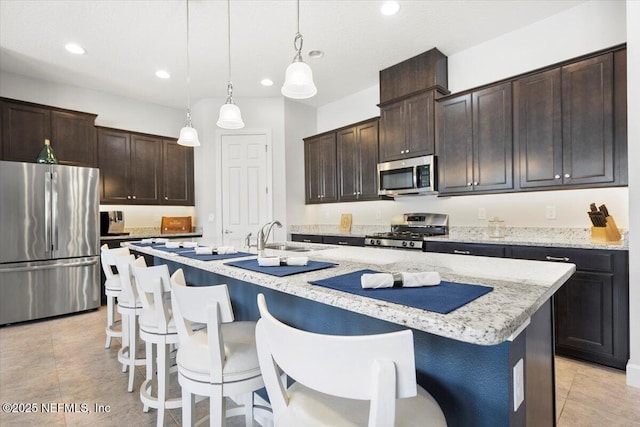 kitchen featuring an island with sink, appliances with stainless steel finishes, sink, and decorative light fixtures