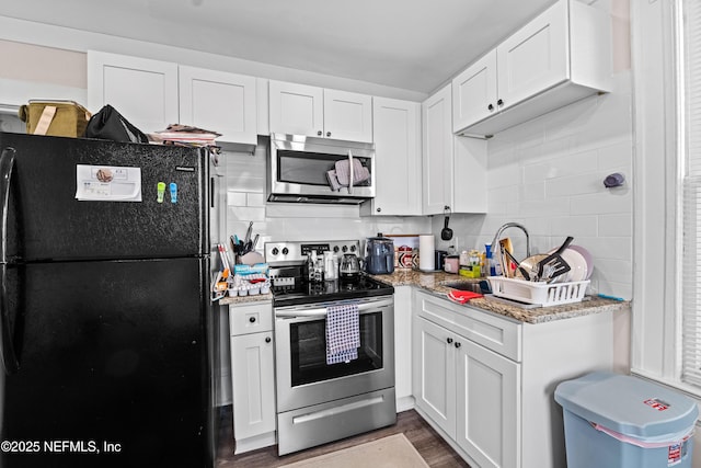 kitchen with sink, appliances with stainless steel finishes, white cabinetry, dark hardwood / wood-style floors, and light stone counters