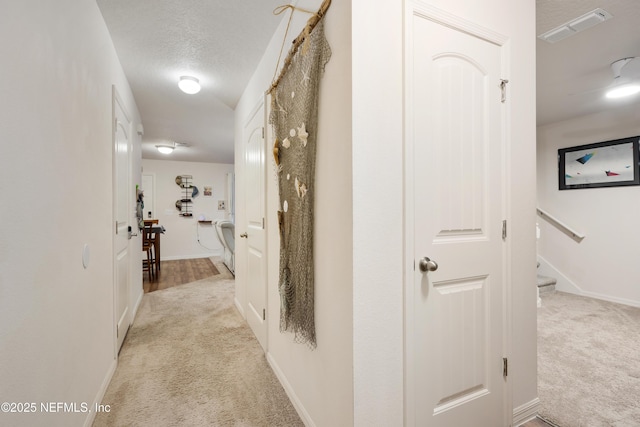 hall featuring light colored carpet and a textured ceiling