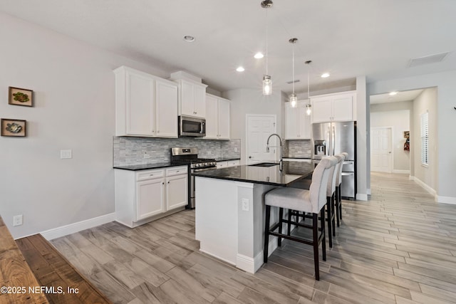 kitchen featuring a kitchen island with sink, white cabinetry, decorative light fixtures, and appliances with stainless steel finishes