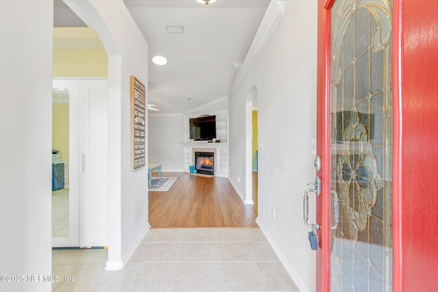 tiled entrance foyer featuring a fireplace with flush hearth, ornamental molding, arched walkways, and baseboards