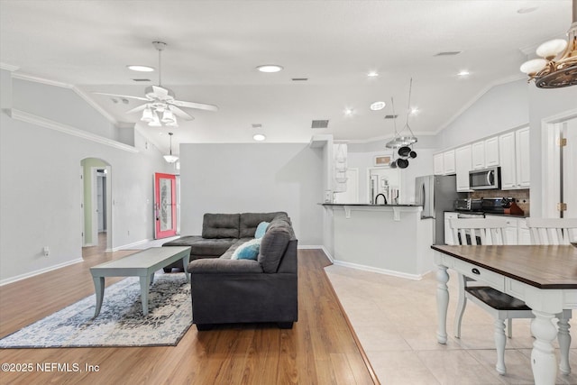 living area with lofted ceiling, a ceiling fan, arched walkways, and crown molding