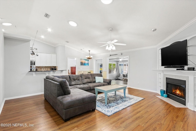 living room featuring crown molding, visible vents, a tiled fireplace, vaulted ceiling, and wood finished floors