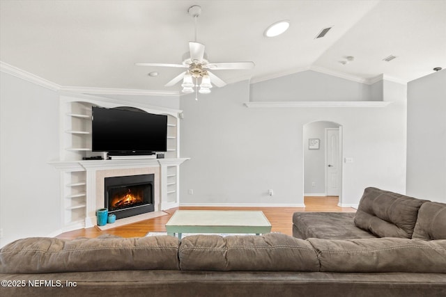 living room featuring arched walkways, light wood finished floors, vaulted ceiling, and a tiled fireplace