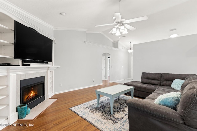 living room with arched walkways, a tile fireplace, lofted ceiling, ornamental molding, and wood finished floors