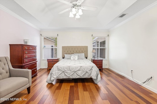 bedroom with a raised ceiling, visible vents, baseboards, and hardwood / wood-style flooring