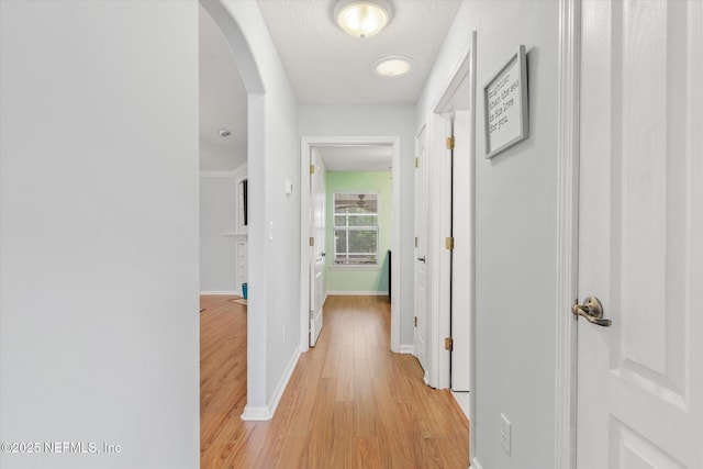 hall with light wood-style floors, baseboards, arched walkways, and a textured ceiling