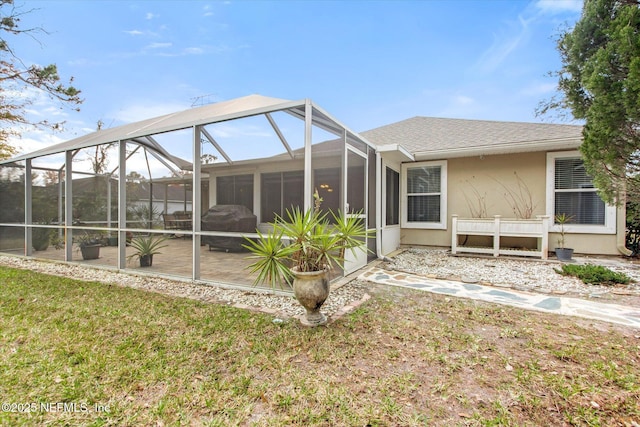 rear view of property featuring a lanai, a yard, roof with shingles, and stucco siding