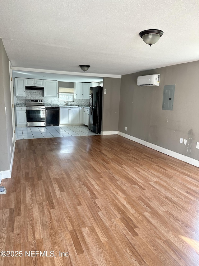 unfurnished living room with a textured ceiling, a wall mounted AC, electric panel, and light hardwood / wood-style floors