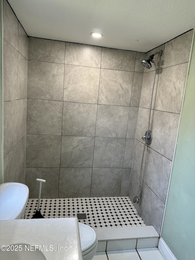 bathroom featuring tile patterned flooring, a tile shower, a textured ceiling, and toilet