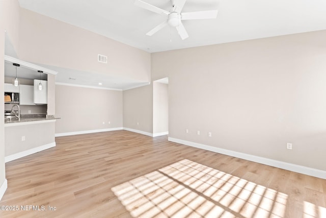 unfurnished living room with sink, vaulted ceiling, light hardwood / wood-style floors, and ceiling fan