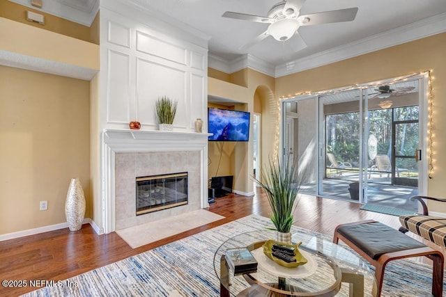 living room featuring crown molding, ceiling fan, a tiled fireplace, and hardwood / wood-style floors