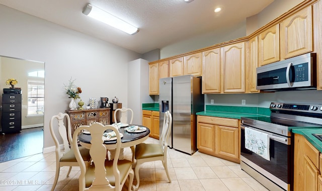 kitchen with light tile patterned floors, stainless steel appliances, a textured ceiling, and light brown cabinets