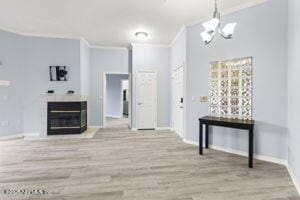 unfurnished living room featuring a fireplace, wood finished floors, baseboards, ornamental molding, and an inviting chandelier