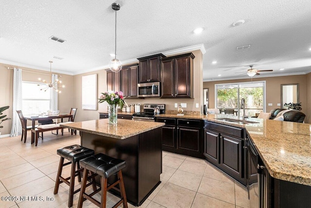 kitchen featuring sink, decorative light fixtures, a center island, ornamental molding, and appliances with stainless steel finishes